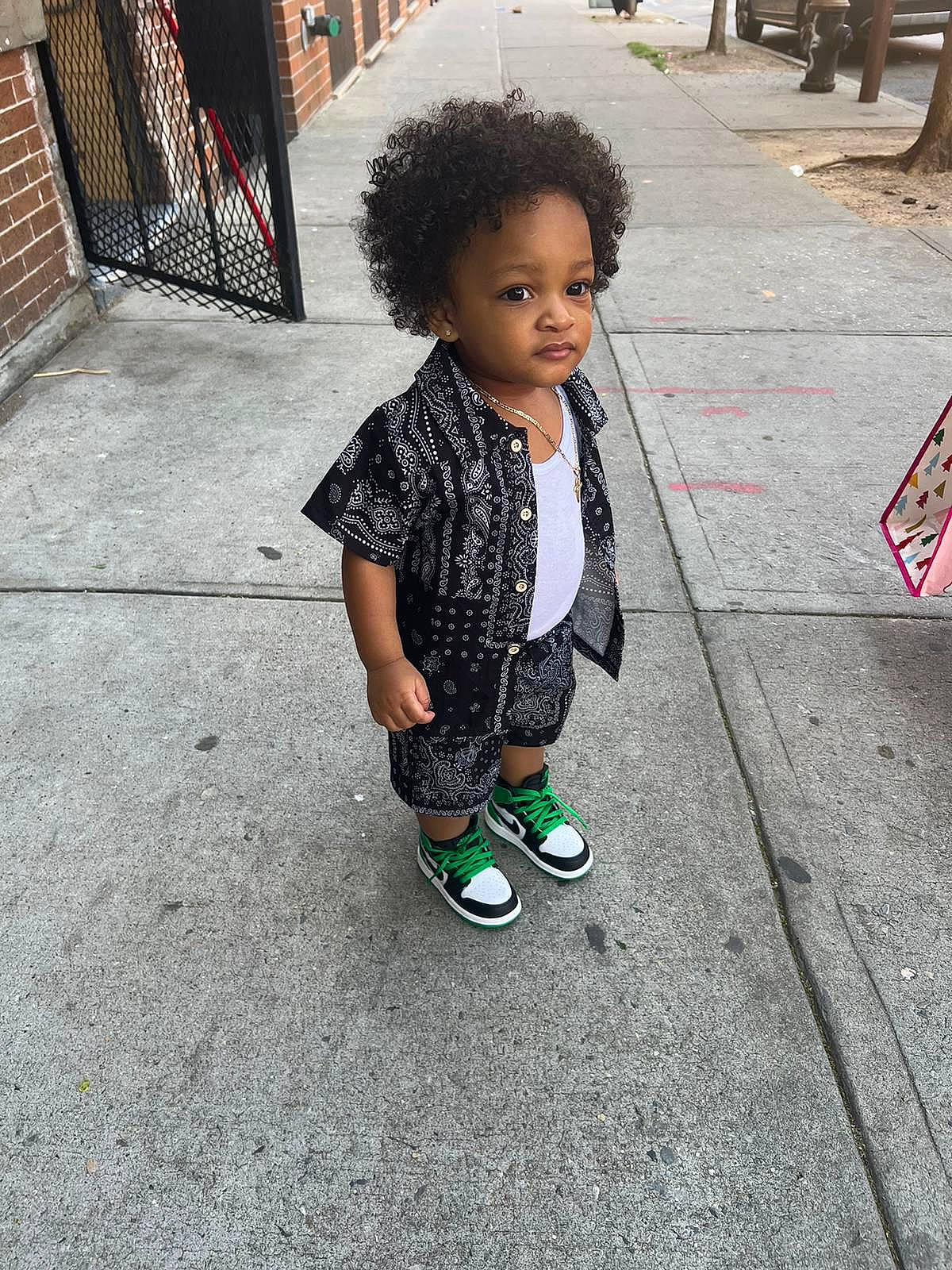 Josiah is registered to the contest to win money with this photo: asphalt, black, child, city, concrete, cool, face, flooring, hairstyle, pedestrian, person, public_space, road, road_surface, shadow, sidewalk, sitting, street, t_shirt, tints_and_shades