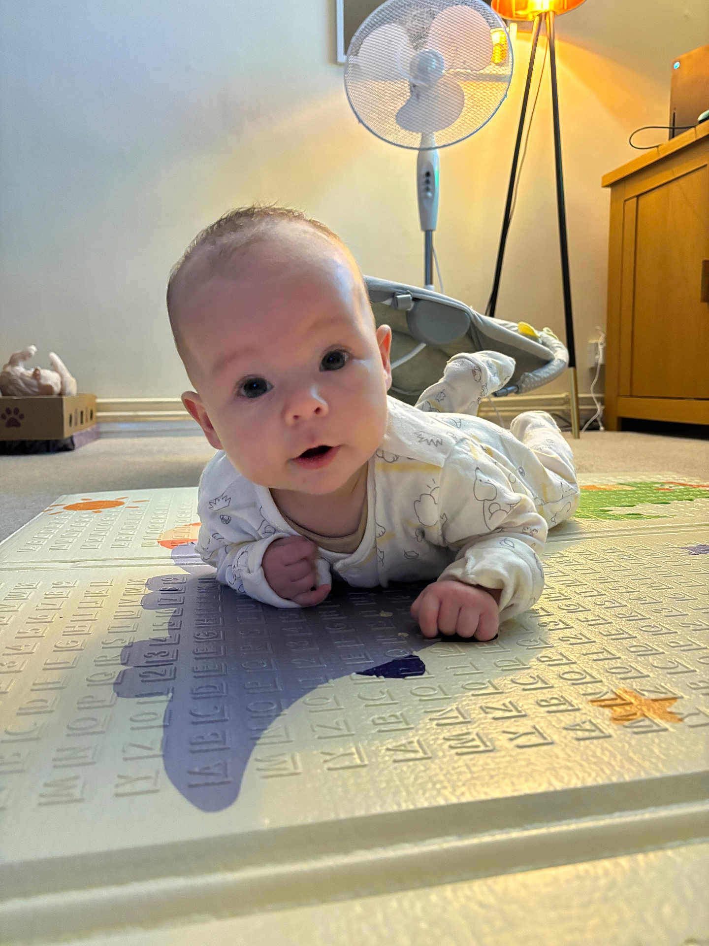 Jensen joined the competition — help win amazing prizes! baby, infant, play_mat, lying_down, indoor, face, curious, wide_eyes, clothing, carpet, fan, lamp, furniture, cabinet, floor, person, child, expression, cute, home