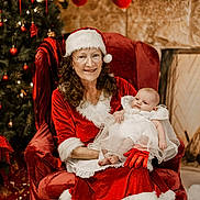 Arabella is registered to the contest to win money with this photo: baby, chair, christmas, christmas_tree, decorations, festive, fireplace, fur_trim, glasses, gloves, holiday, holiday_season, indoor, infant, mrs_claus, red_dress, smile, stockings, white_dress, woman