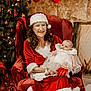 baby, chair, christmas, christmas_tree, decorations, festive, fireplace, fur_trim, glasses, gloves, holiday, holiday_season, indoor, infant, mrs_claus, red_dress, smile, stockings, white_dress, woman