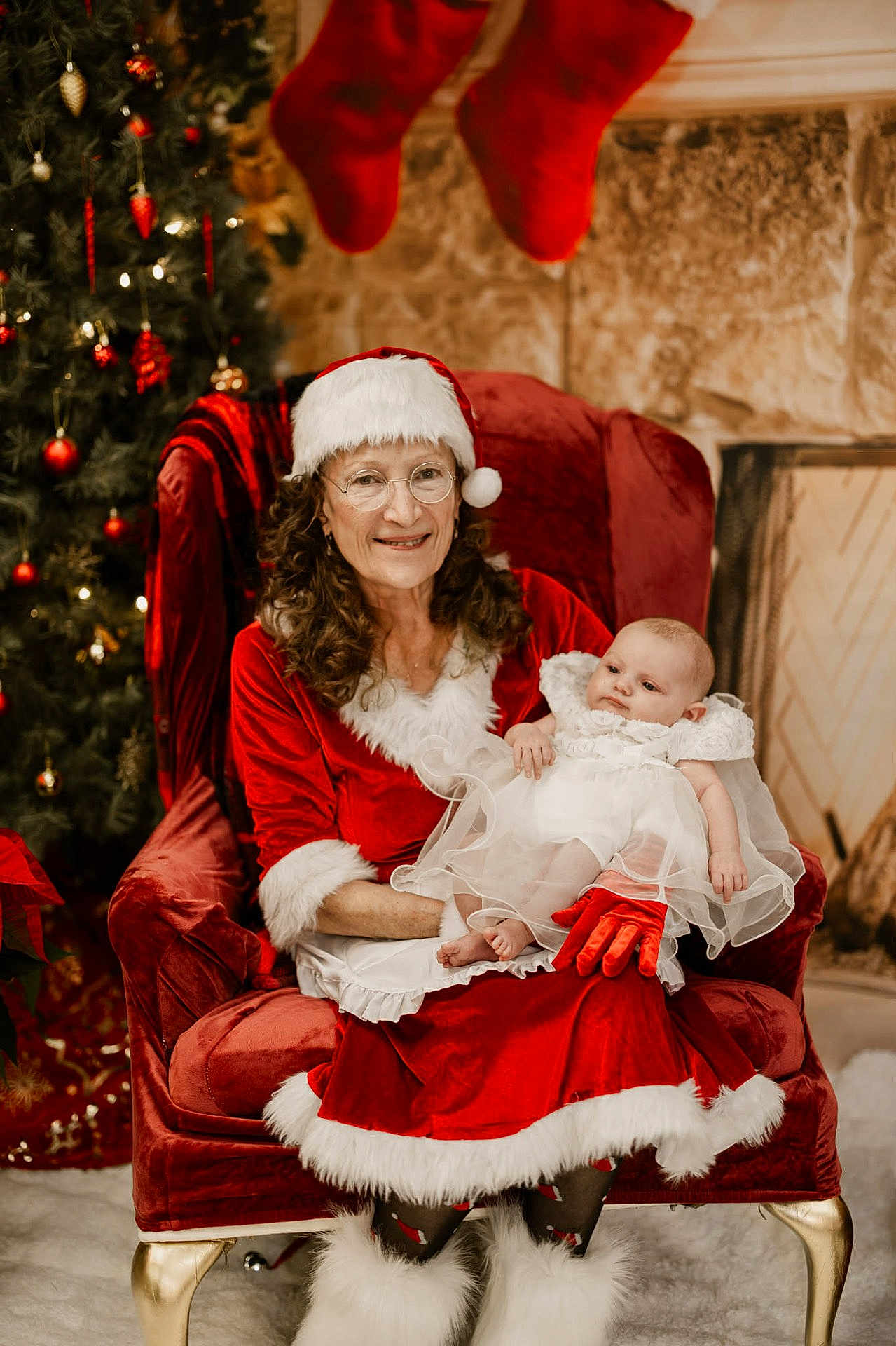Arabella is registered to the contest to win money with this photo: baby, chair, christmas, christmas_tree, decorations, festive, fireplace, fur_trim, glasses, gloves, holiday, holiday_season, indoor, infant, mrs_claus, red_dress, smile, stockings, white_dress, woman