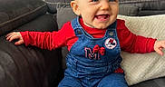 Alba a rejoint le concours — aidez-le/la à gagner de superbes lots ! toddler, child, smiling, sitting, couch, overalls, red_clothing, blue_clothing, pigtails, baby, indoor, happy, face, person, sock, furniture, dartboard, home, cute, portrait