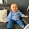 toddler, child, blue_eyes, pony_tail, blue_blouse, jeans, sneakers, couch, pillow, indoor, smiling, casual_clothing, young_child, cute, seated, home, portrait, face, happy, relaxed