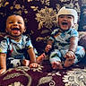 baby, babies, child, smiling, laughing, sitting, pajamas, helmet, couch, patterned_fabric, indoor, happy, cute, infant, two_children, joy, portrait, playful, family, comfort