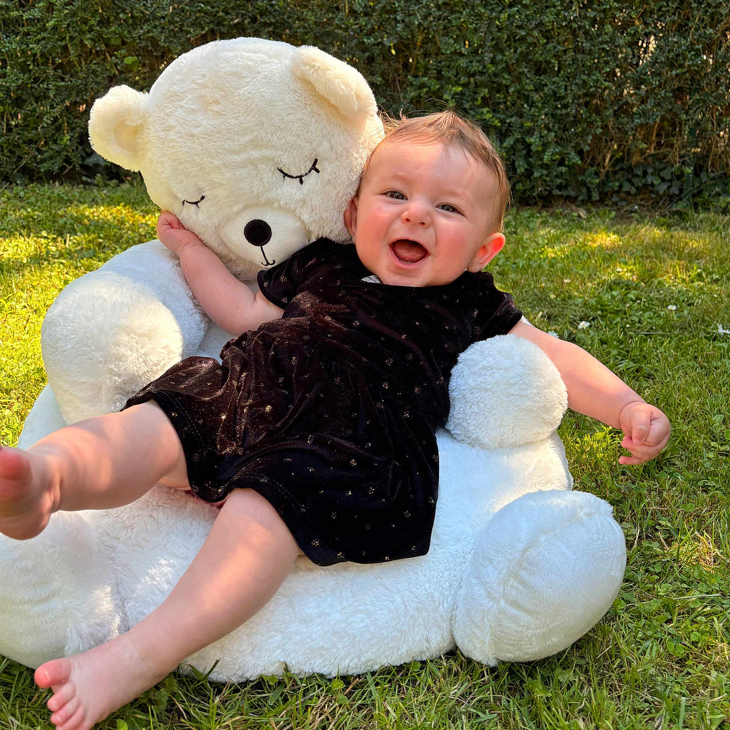 Maëlle a rejoint le concours — aidez-le/la à gagner de superbes lots ! baby, teddy_bear, outdoor, grass, smiling, child, plush, hedge, greenery, sunlight, cute, playing, happy, black_clothing, feet, toy, nature, summer, infant, portrait
