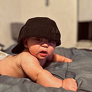 Hayden is registered to the contest to win money with this photo: baby, baseballcap, bed, bedroom, bodypart, cap, clothing, face, finger, furniture, hand, happy, hat, head, indoors, person, photography, portrait, room, smile