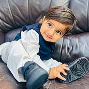 Gurupdesh joined the competition — help win amazing prizes! toddler, child, smile, shoe, black_shoe, white_clothing, navy_vest, leather_couch, indoor, cute, portrait, happy, young_child, hand, footwear, sitting, face, big_eyes, curly_hair, playful