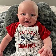 Wylder is registered to the contest to win money with this photo: baby, infant, smiling, clothing, red_shirt, striped_outfit, blanket, indoor, portrait, happy, cute, child, baby_hand, sitting, face, person, soft_texture, comfort, young, casual