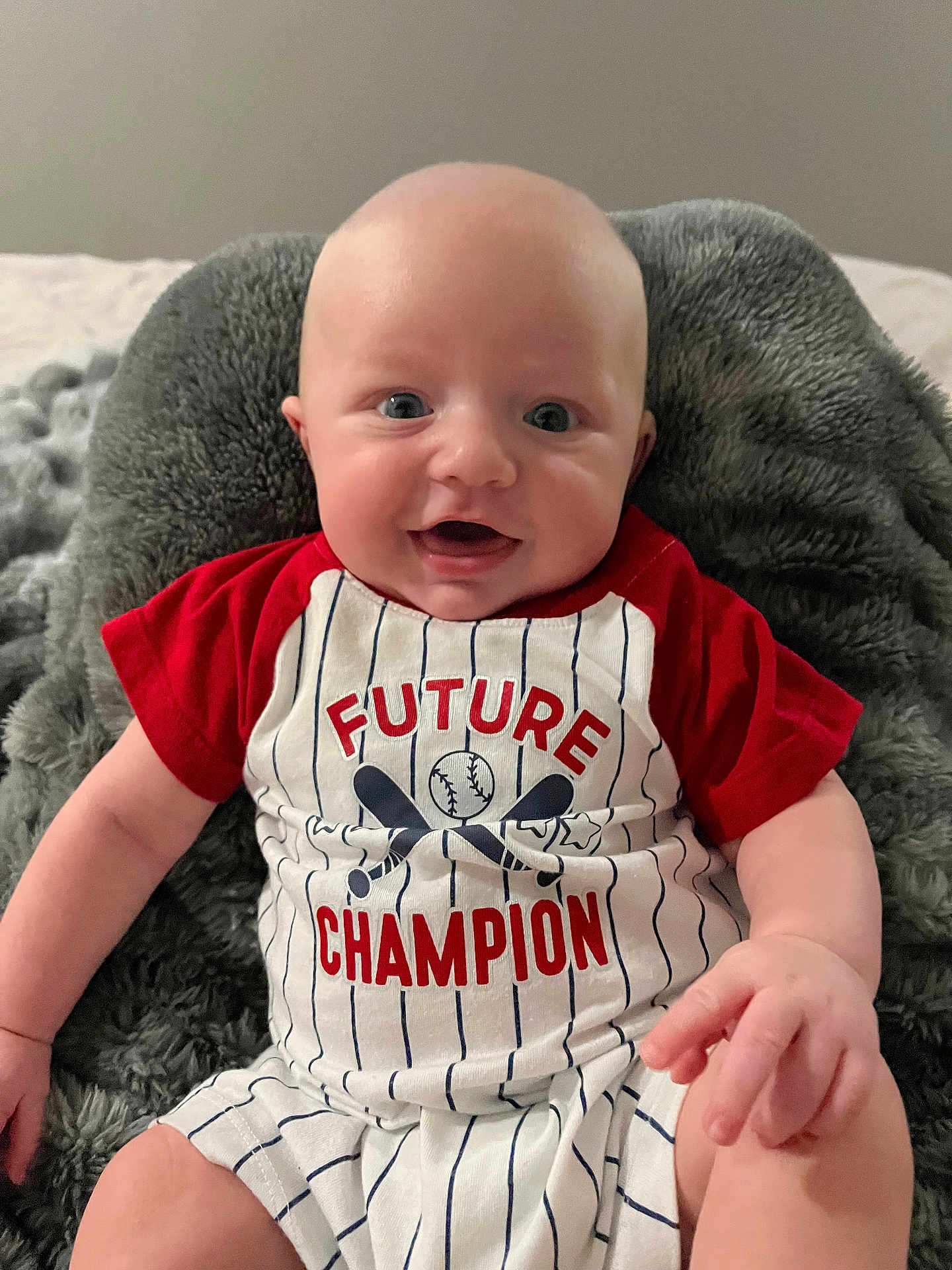 Wylder is registered to the contest to win money with this photo: baby, infant, smiling, clothing, red_shirt, striped_outfit, blanket, indoor, portrait, happy, cute, child, baby_hand, sitting, face, person, soft_texture, comfort, young, casual