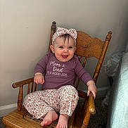 Evelyn joined the competition — help win amazing prizes! baby, child, smiling, rocking_chair, wooden_chair, headband, floral_pattern, purple_clothing, long_sleeve, pants, barefoot, indoor, carpet, happy, cute, person, sitting, infant, portrait, home