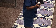 Omarius joined the competition — help win amazing prizes! toddler, child, indoor, carpet, floral_pattern, navy_blue_clothing, shorts, shirt, white_sneakers, curious_expression, holding_object, runner, chair, carpeted_floor, earring, person, standing, looking_back, black_hair, small_object