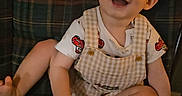 Raylan is registered to the contest to win money with this photo: baby, child, cute, face, foot, hand, happy, indoor, infant, months_marker, overalls, person, plaid_chair, portrait, red_design, sitting, smiling, white_shirt, wooden_plaque, young