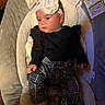 baby, black_outfit, blanket, child, cushion, face, fashion, flower, headband, home, houndstooth_pants, indoor, infant, infant_seat, looking_away, portrait, ruffled_sleeves, safe_sleep_warning, sitting, socks