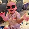 Liam is registered to the contest to win money with this photo: toddler, child, sunglasses, smiling, happy, indoor, playmat, striped_clothing, shorts, shirt, red, living_room, couch, pillow, carpet, toy, baby, person, cute, fun