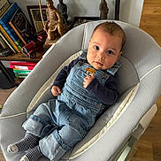 Theo a rejoint le concours — aidez-le/la à gagner de superbes lots ! baby, infant, denim_overalls, striped_socks, baby_bouncer, baby_seat, bookshelf, books, wooden_statue, toy_car, indoor, hardwood_floor, face, big_eyes, curious_expression, hand, cozy, portrait, clothing, cute