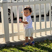 Thiago joined the competition — help win amazing prizes! toddler, child, white_picket_fence, grass, sunlight, outdoor, car, curious, shorts, tshirt, socks, shoes, side_view, standing, daytime, shadow, nature, portrait, playful, young_child