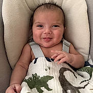 Eli is registered to the contest to win money with this photo: baby, infant, smile, face, blanket, dinosaur, cushion, seat, happy, cute, child, portrait, clothing, hand, skin, young, indoors, expression, comfort, cozy