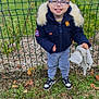 Lyam participe au concours pour gagner de l'argent avec cette photo : child, smiling, eyeglasses, navy_jacket, fur_hood, gray_sweatpants, sneakers, green_fence, grass, leaves, holding_blanket, soft_toy, outdoor, backyard, portrait, standing, happy, short_hair, mulch, residential_background