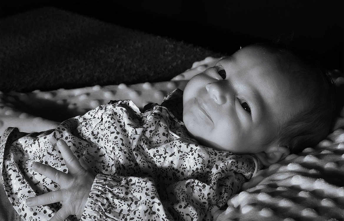 Mia participe au concours pour gagner de l'argent avec cette photo : baby, newborn, infant, face, smile, eyes, hand, blanket, bedding, patterned_clothing, monochrome, black_and_white, portrait, soft_texture, lying_down, cute, newborn_clothes, cheek, head, cozy