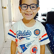 Eduardo joined the competition — help win amazing prizes! child, boy, glasses, smile, tshirt, spiky_hair, indoor, living_room, couch, tile_floor, door, window, happy, portrait, person, casual_clothing, young, home, bright, standing