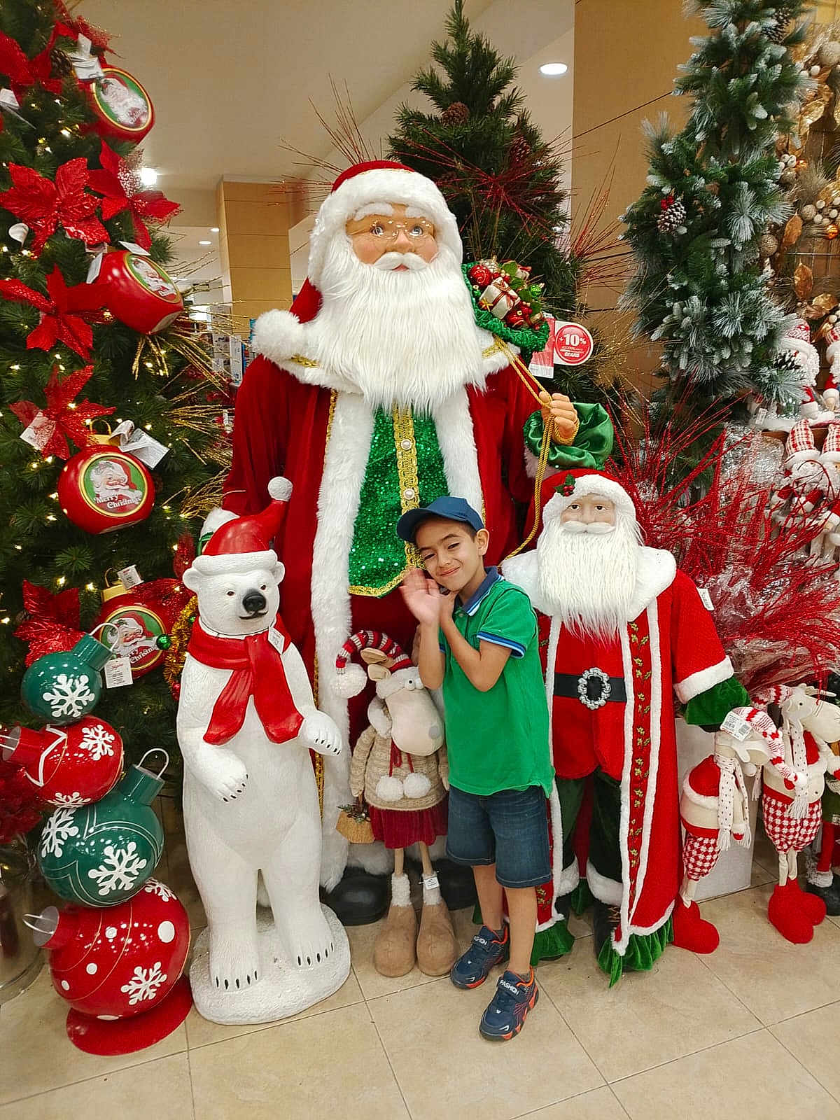 Eduardo joined the competition — help win amazing prizes! child, boy, green_shirt, blue_cap, santa_claus, polar_bear_statue, christmas_tree, christmas_decorations, holiday, festive, shopping_mall, decorative_figures, smiling, posing, indoor, floor_tiles, red_scarf, plush_toys, seasonal, happy