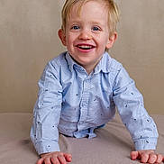 Gabriel participe au concours pour gagner de l'argent avec cette photo : child, boy, smiling, happy, blue_eyes, blonde_hair, shirt, long_sleeves, patterned_clothing, blanket, indoor, portrait, cute, young_child, toddler, face, hands, neutral_background, playful, joyful