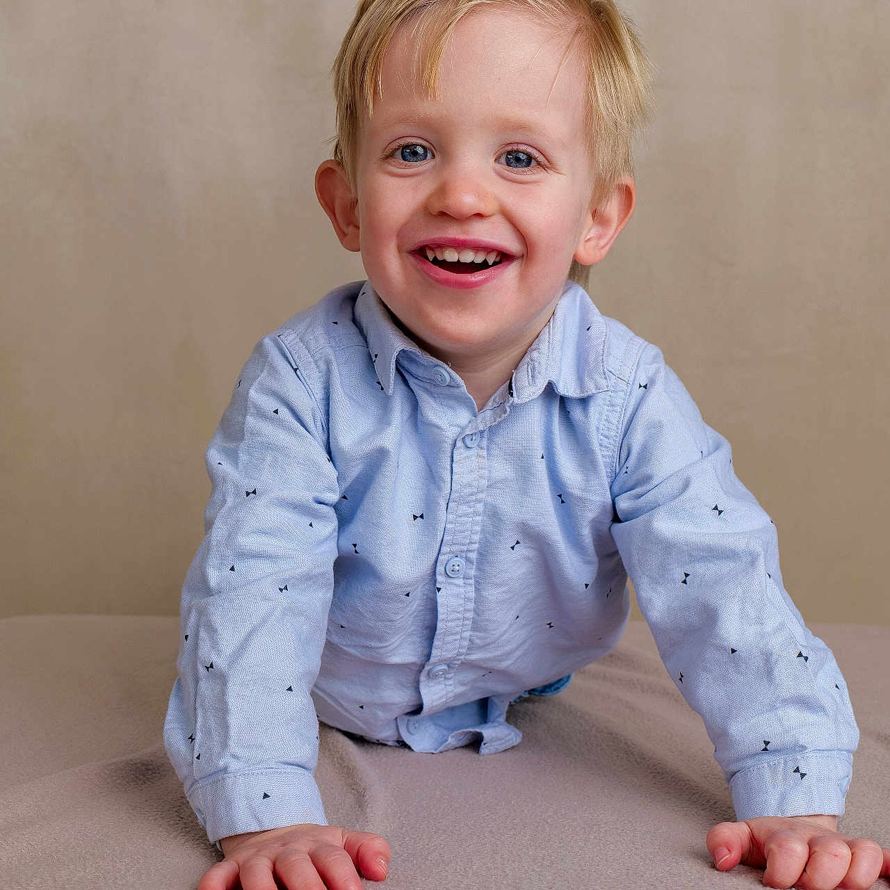 Gabriel participe au concours pour gagner de l'argent avec cette photo : blanket, blonde_hair, blue_eyes, boy, child, cute, face, hands, happy, indoor, joyful, long_sleeves, neutral_background, patterned_clothing, playful, portrait, shirt, smiling, toddler, young_child