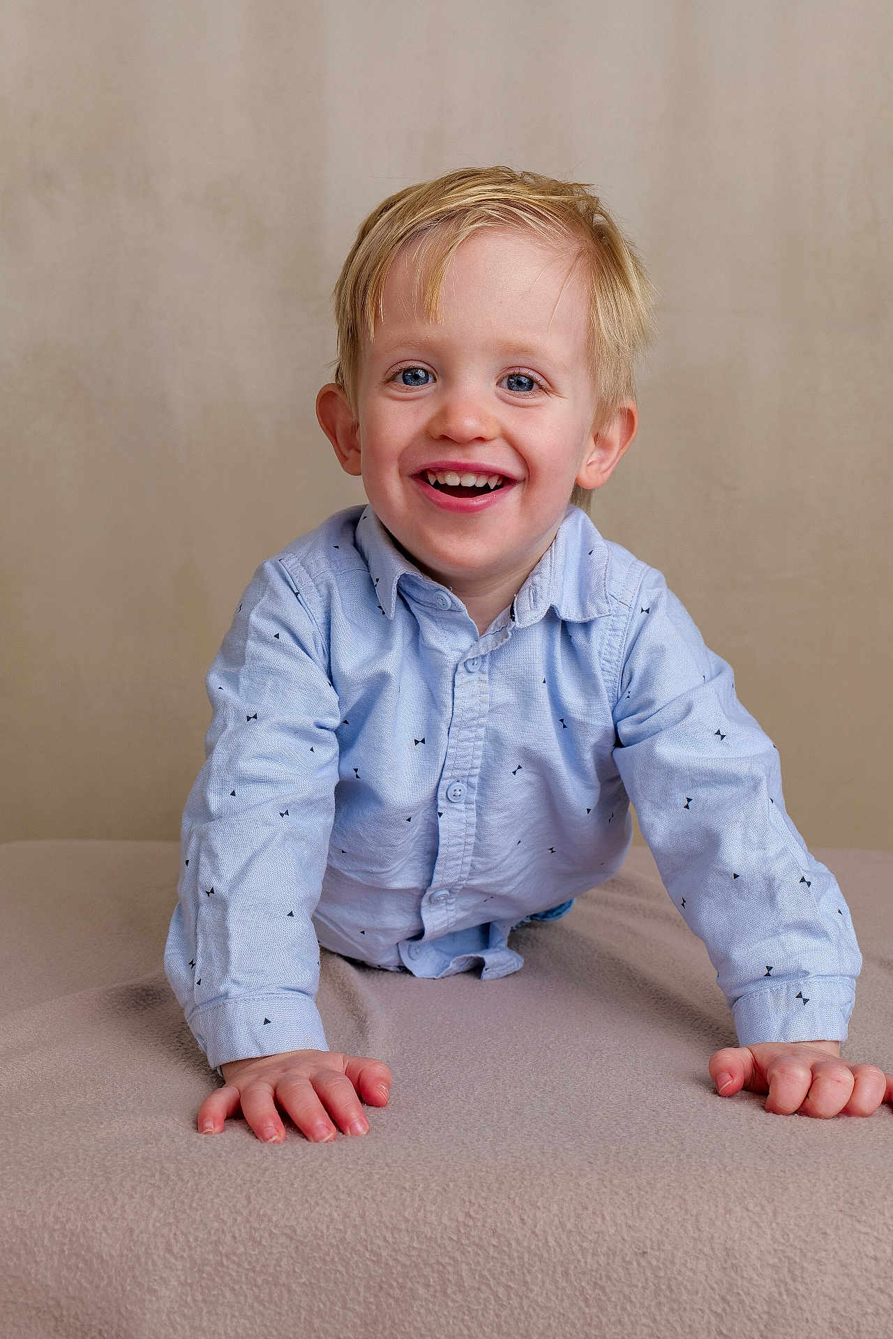 Gabriel participe au concours pour gagner de l'argent avec cette photo : child, boy, smiling, happy, blue_eyes, blonde_hair, shirt, long_sleeves, patterned_clothing, blanket, indoor, portrait, cute, young_child, toddler, face, hands, neutral_background, playful, joyful