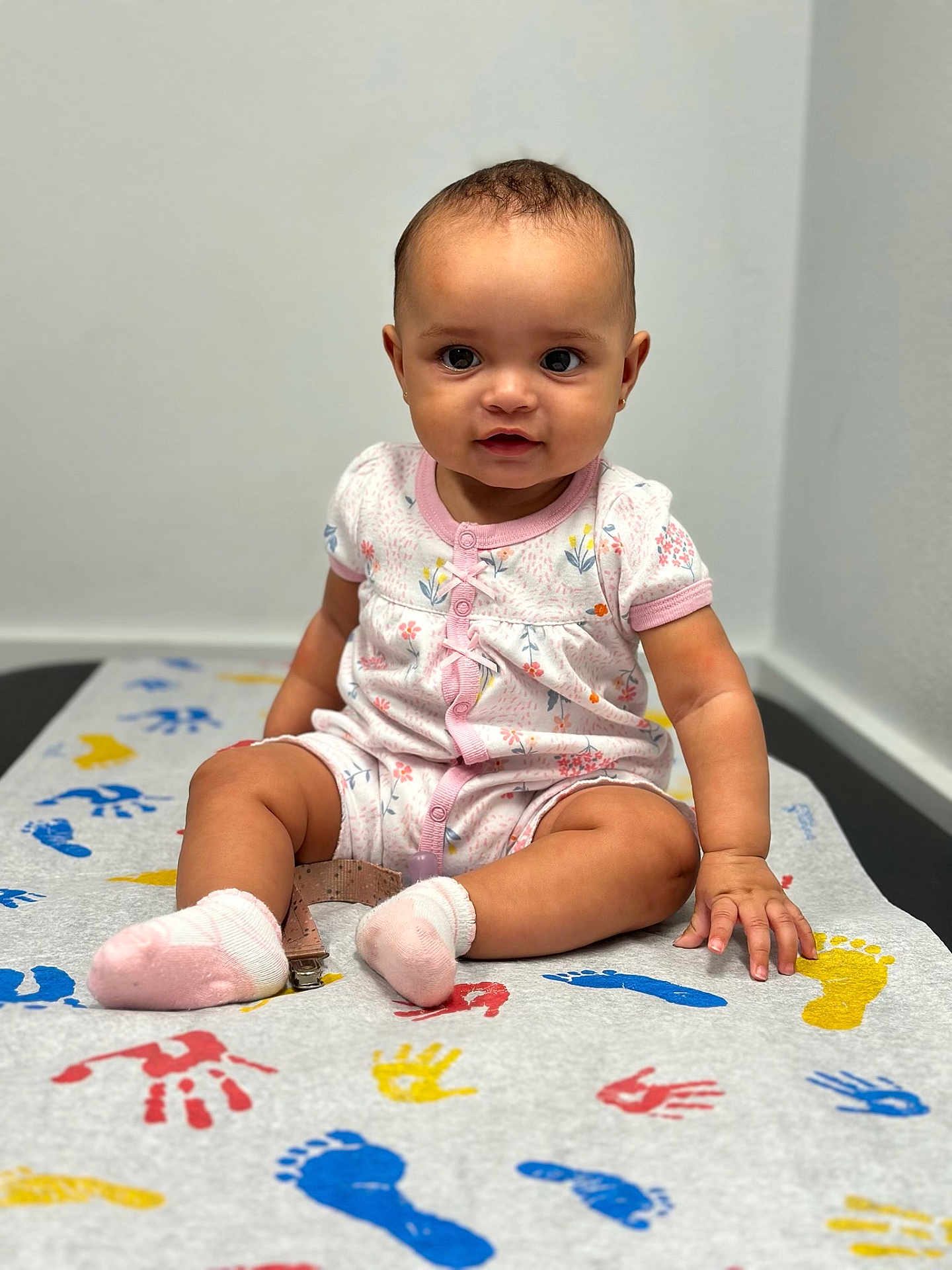 Belen is registered to the contest to win money with this photo: baby, child, infant, sitting, onesie, pink, socks, handprints, footprints, colorful, table, floor, indoor, curious, cute, portrait, skin, face, person, young