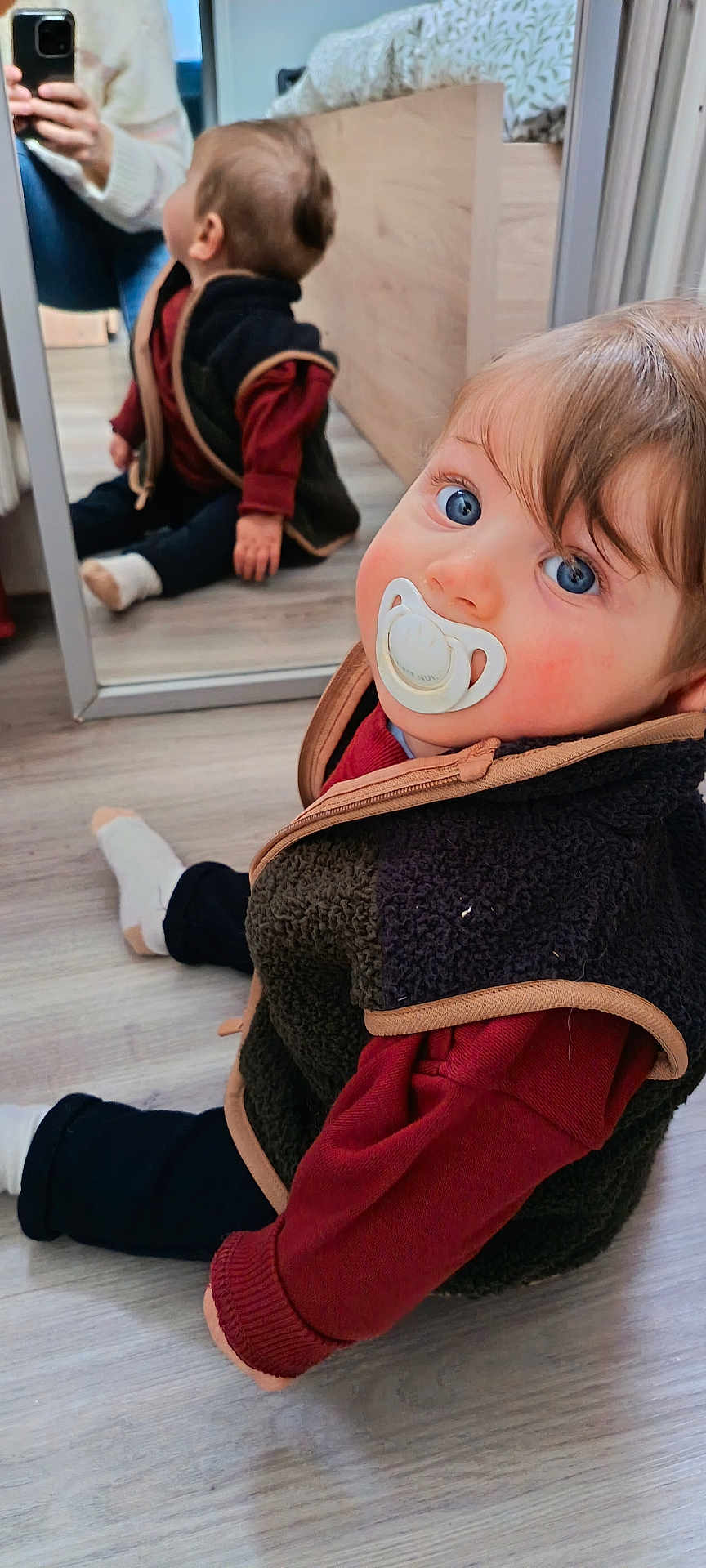 Maël a rejoint le concours — aidez-le/la à gagner de superbes lots ! baby, pacifier, blue_eyes, reflection, mirror, fleece_vest, red_sweater, sitting, wooden_floor, indoor, child, person, hand, footwear, casual_clothing, cozy, home, cute, portrait, photography