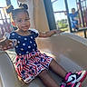 child, girl, toddler, playground, slide, outdoor, portrait, smiling, sitting, dress, stars, patriotic, sneakers, pink_shoes, playground_equipment, sunlight, daytime, blurred_background, hair_buns, happy