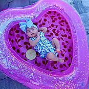 Alanna is registered to the contest to win money with this photo: baby, infant, sleeping, heart_shaped_pool, inflatable, pink, blue_bow, floral_outfit, towel, cherry_pattern, outdoor, pavement, wooden_plaque, age_marker, cute, peaceful, child, portrait, sparkly, relaxing