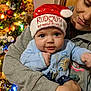 baby, child, adult, christmas_tree, holiday, festive_hat, rudolph, red_nose, reindeer, smiling, blue_clothing, indoor, warm_lighting, celebration, family, portrait, holding, face, eyes, happy