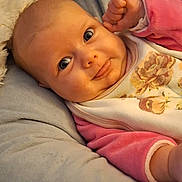 Yris a rejoint le concours — aidez-le/la à gagner de superbes lots ! baby, cheek, closeup, clothing, cushion, cute, eyes, face, floral_bib, hand, indoors, infant, lying_down, pink_sleeves, portrait, relaxing, skin, smile, soft_texture, tongue