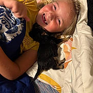 Mika is registered to the contest to win money with this photo: child, smiling, bed, blanket, puppy, dog, pet, lying_down, yellow_shirt, happy, indoor, cute, cozy, friendship, snuggling, sleeping, animal, person, face, hair