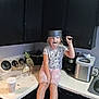 Mika is registered to the contest to win money with this photo: child, kitchen, counter, pot, playful, tongue_out, appliance, coffee_maker, ice_maker, cup, cabinet, girl, casual_clothing, sitting, funny_face, home, indoor, light, person, barefoot