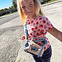 child, blonde_hair, pink_shirt, strawberry_pattern, striped_leggings, small_bag, stitch_character, outdoor, sunlight, sidewalk, street, trees, houses, blue_sky, smiling, person, standing, casual_clothing, daytime, accessory