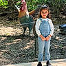 Aadvi joined the competition — help win amazing prizes! child, girl, denim_overalls, forest, statue, rooster, outdoor, nature, sunlight, trees, pathway, shoes, posing, daylight, greenery, smiling, person, casual_clothing, sculpture, background