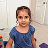 child, girl, blue_clothing, curly_hair, indoor, carpet, magnetic_tiles, toys, door, white_wall, sitting, portrait, young, play, casual, looking_at_camera, cute, floor, home, smile