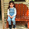 Aadvi joined the competition — help win amazing prizes! child, girl, bench, wooden_bench, overalls, denim, white_sweater, outdoor, cabin, wooden_cabin, curly_hair, black_shoes, portrait, smiling, sitting, daylight, nature, rustic, cute, young