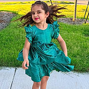Aadvi is registered to the contest to win money with this photo: child, girl, dress, green_dress, toddler, happy, smiling, hair, long_hair, outdoor, sidewalk, grass, lawn, suburb, street, sneakers, playful, sunlight, portrait, person