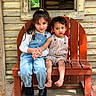 children, girl, boy, bench, wooden_bench, holding_hands, outdoor, sunlight, smiling, curious, rustic, wooden_wall, overalls, casual_clothing, barefoot, long_hair, short_hair, siblings, nature, portrait
