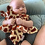 Jack is registered to the contest to win money with this photo: baby, infant, plush_toy, giraffe_pattern, cushion, carpet, clothing, legs, hands, soft_toy, child, cute, indoor, person, comfort, relaxing, expression, seated, skin, closeup