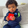toddler, child, nike, tracksuit, jbl, speaker, couch, indoor, curly_hair, sitting, black_socks, cozy, beige, fabric, young_child, person, clothing, expression, holding, furniture