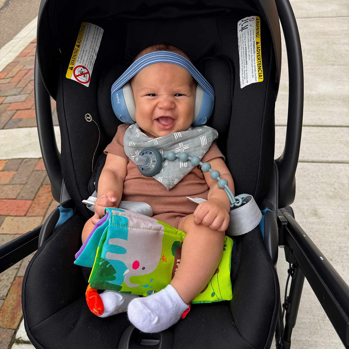 Kenzo joined the competition — help win amazing prizes! baby, stroller, car_seat, headphones, bib, toy, cloth_book, smile, happy, infant, outdoor, sidewalk, person, footwear, sock, clothing, hand, face, seatbelt, black
