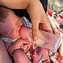 baby, feeding, bottle, hand, foot, infant, newborn, person, blanket, clothing, skin, nourishment, care, closeup, indoors, soft_lighting, human, parent, rest, comfort