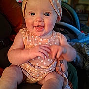 Aura is registered to the contest to win money with this photo: baby, child, polka_dot, headband, smile, drool, sitting, person, hand, tattoo, indoors, clothing, infant, cute, happy, skin, furniture, blurred_background, warm_lighting, portrait