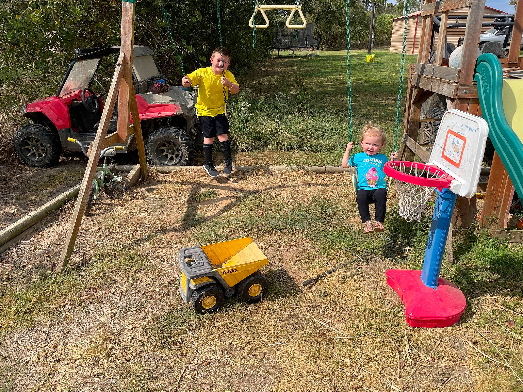 Brayden is registered to the contest to win money with this photo: asphalt, car, fun, garden_tool, grass, green, joy, lawn, motor_vehicle, nature, person, plant, public_space, recreation, rural_area, tire, tree, vehicle, wheel, wheelbarrow