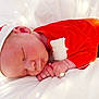 baby, sleeping, infant, red_clothing, santa_hat, pom_pom, fairy_lights, white_background, holiday, festive, cute, soft_texture, peaceful, newborn, close_up, portrait, christmas, hands, face, resting
