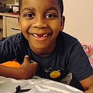 Oshea is registered to the contest to win money with this photo: child, smiling, boy, face, indoor, blanket, furniture, computer, desk, clothing, short_hair, teeth, happy, portrait, person, home, electronics, room, youth, casual